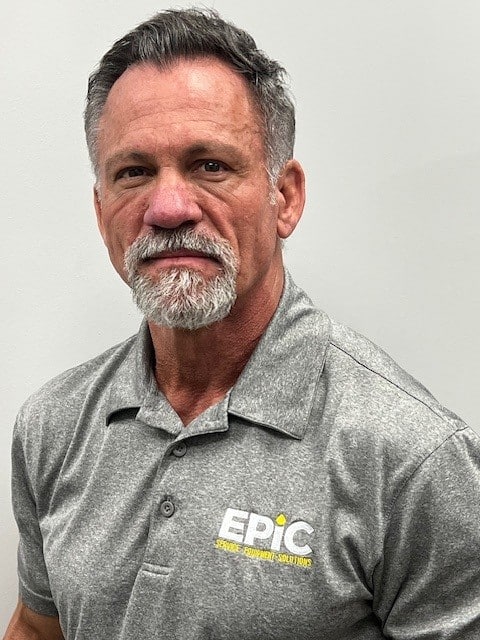 A man with short gray hair and a beard in a gray EPIC shirt stands before a plain light background, facing the camera neutrally.