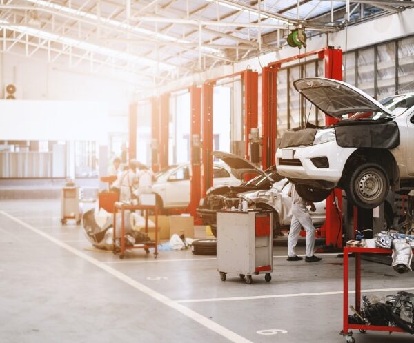 Mechanics working on cars lifted on hydraulic ramps in a spacious, well-lit auto repair shop with tools and car parts organized around the workspace.