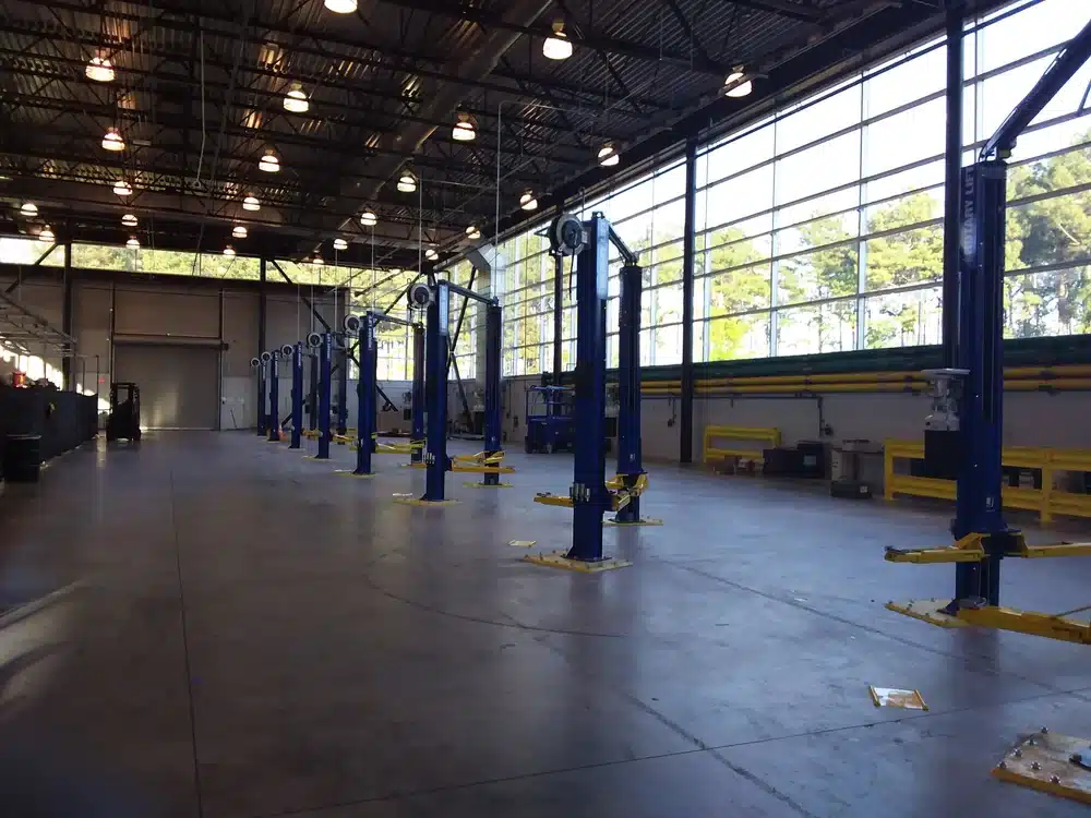 Spacious, well-lit auto repair garage with rows of vehicle lifts, large side windows, and industrial lights on a high ceiling.