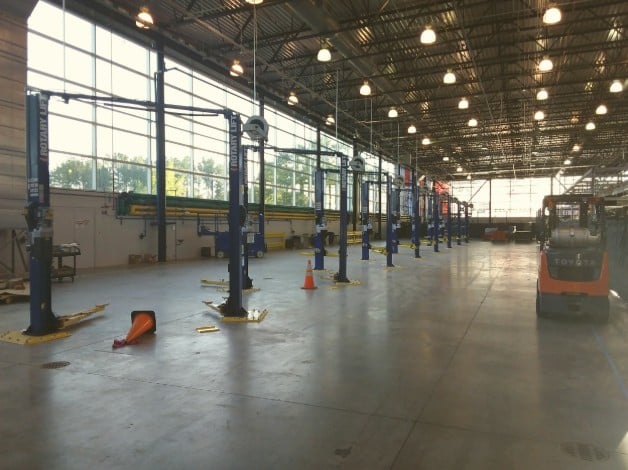 A bright, roomy auto repair shop with several empty lifts, large windows, orange cones on the floor, and a Toyota forklift nearby.