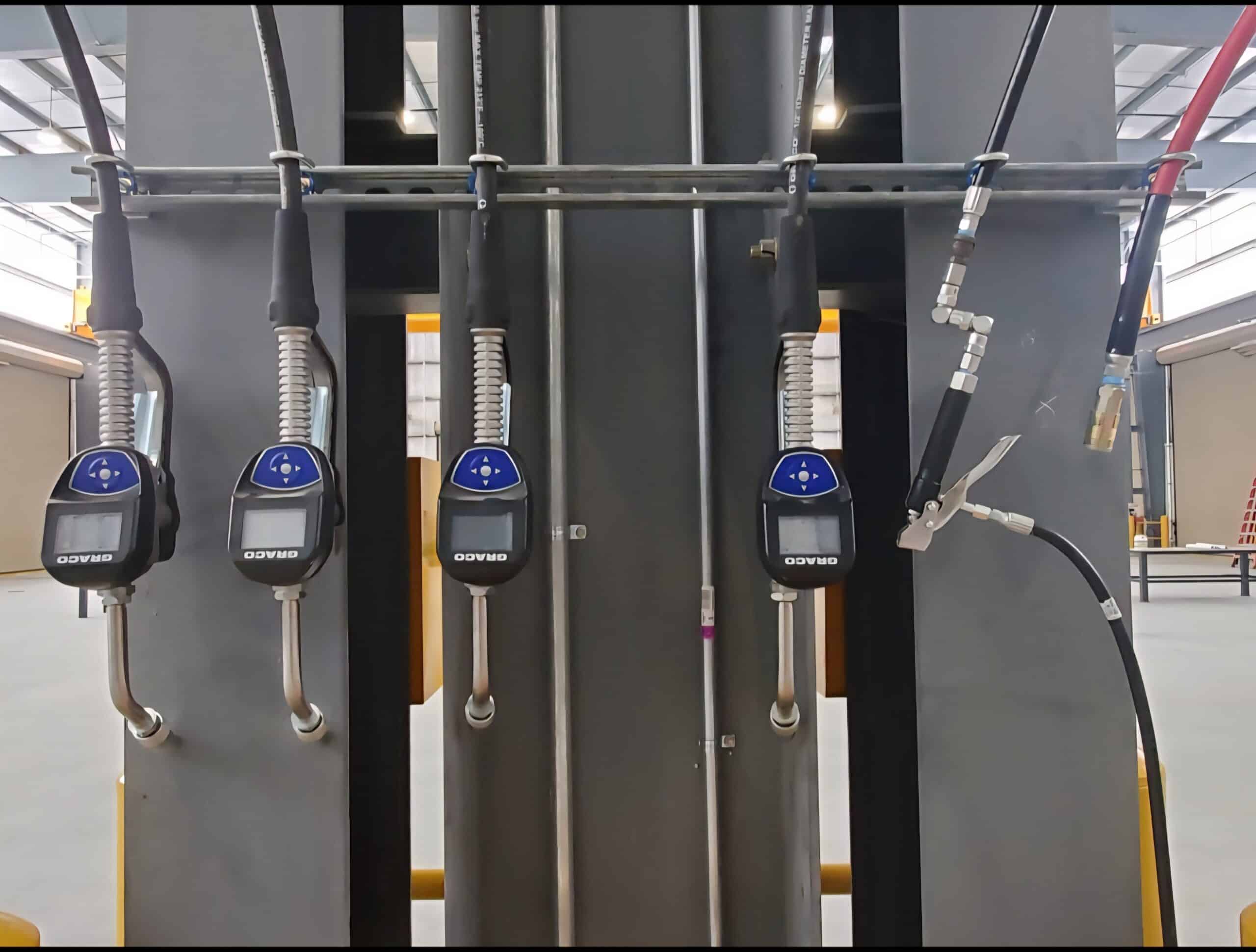 Four fuel or oil dispensing nozzles with digital meters and black hoses on a metal stand indoors, plus two more hoses on the right.