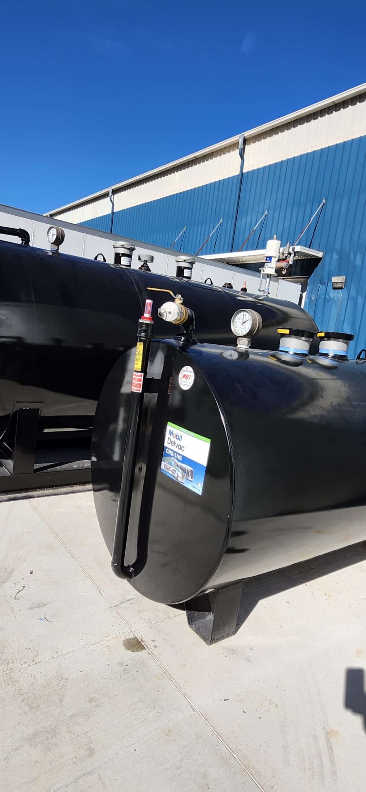 A large black tank with gauges and pipes sits outdoors on concrete near a blue building. A label on the tank reads Model CH-5500VC.