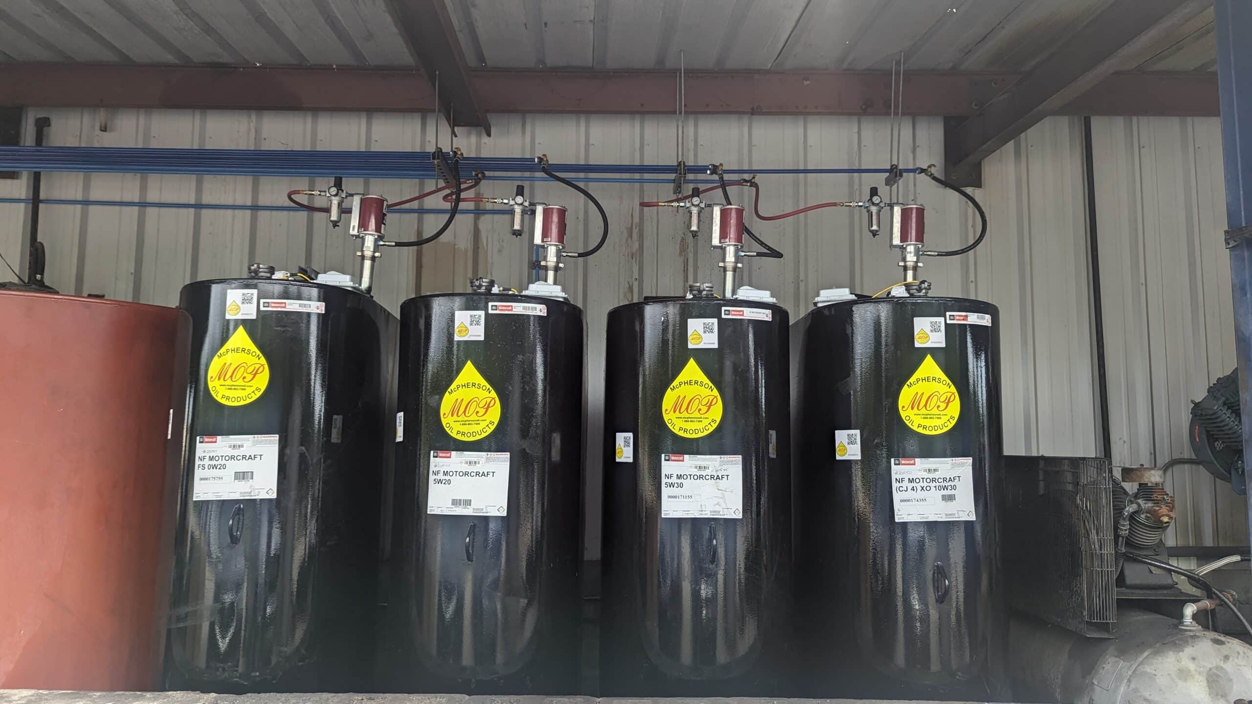 Four large black storage tanks labeled Mid-Continent Oil and Gas with yellow signs stand under a metal shelter, connected by pipes and red equipment.